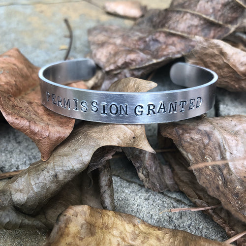 aluminum bracelet with permission granted hand stamped on it. 